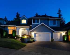 A nice home with two garages and lights on during the final hours of the day.